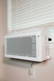 White air conditioner unit mounted in a window with closed white blinds.