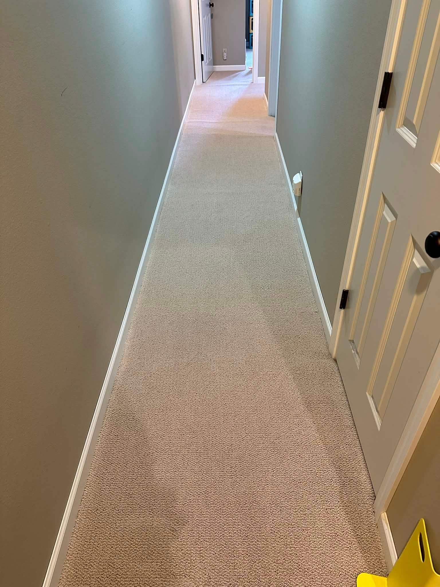 Long carpeted hallway with beige walls and white doors, viewed from one end.