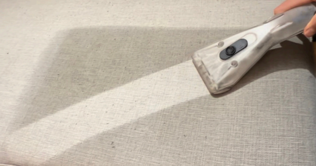 Handheld vacuum cleaning a beige carpet with a diagonal light-and-shadow pattern