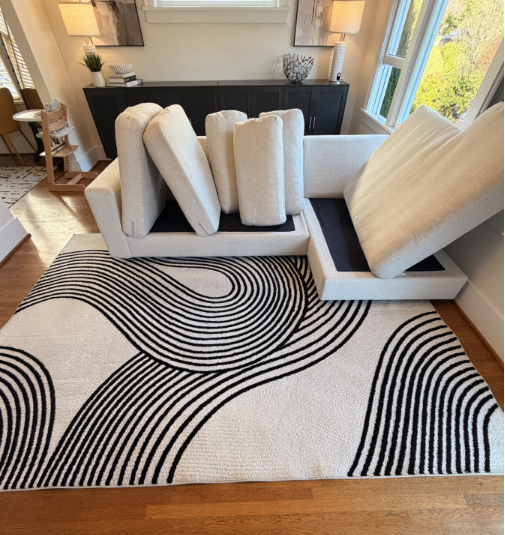 Abstract black-and-white rug in a bright living room with white chairs and a black fireplace mantel
