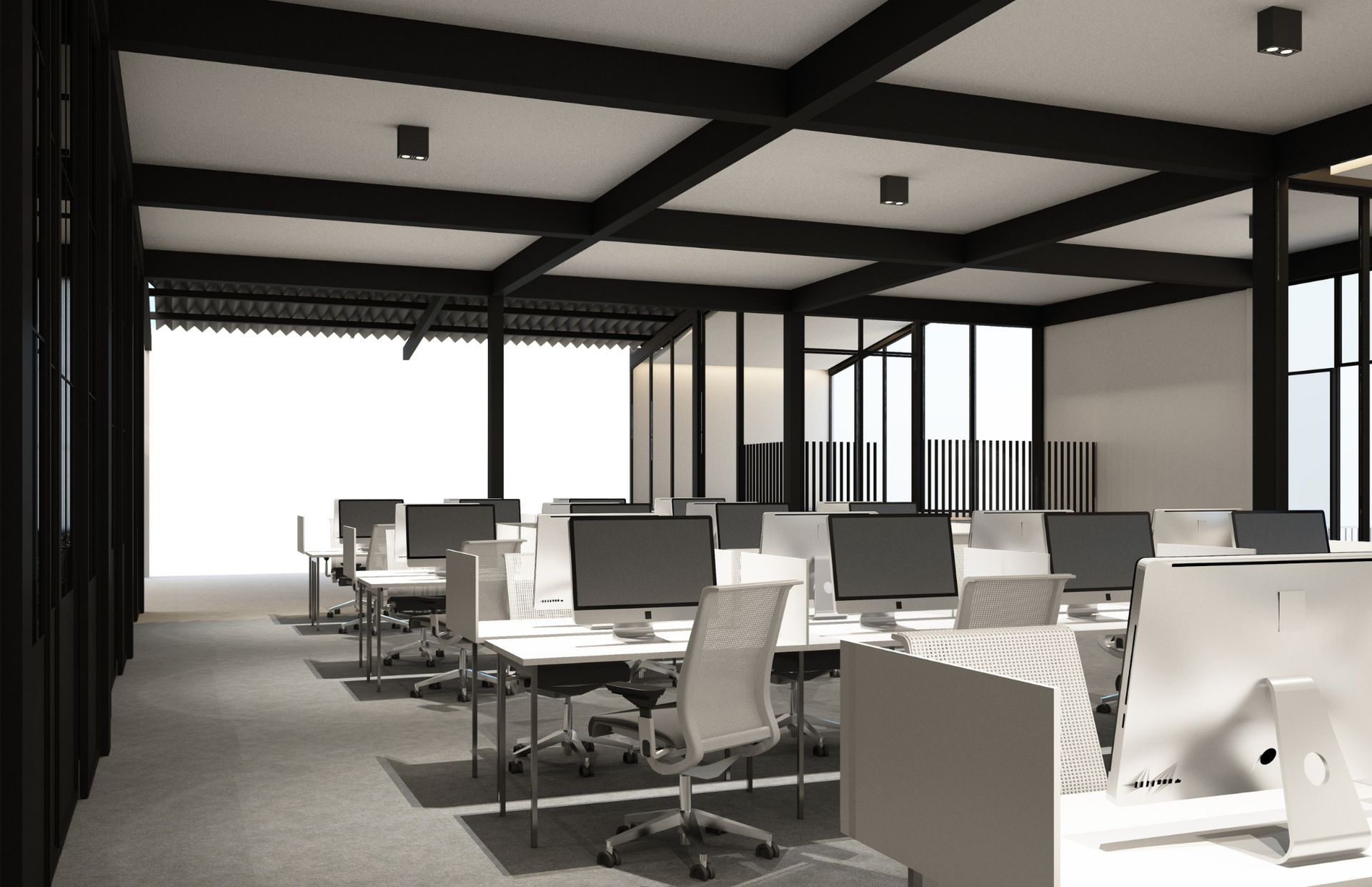 Modern open office with rows of desks, computer monitors, and black ceiling beams in a bright workspace