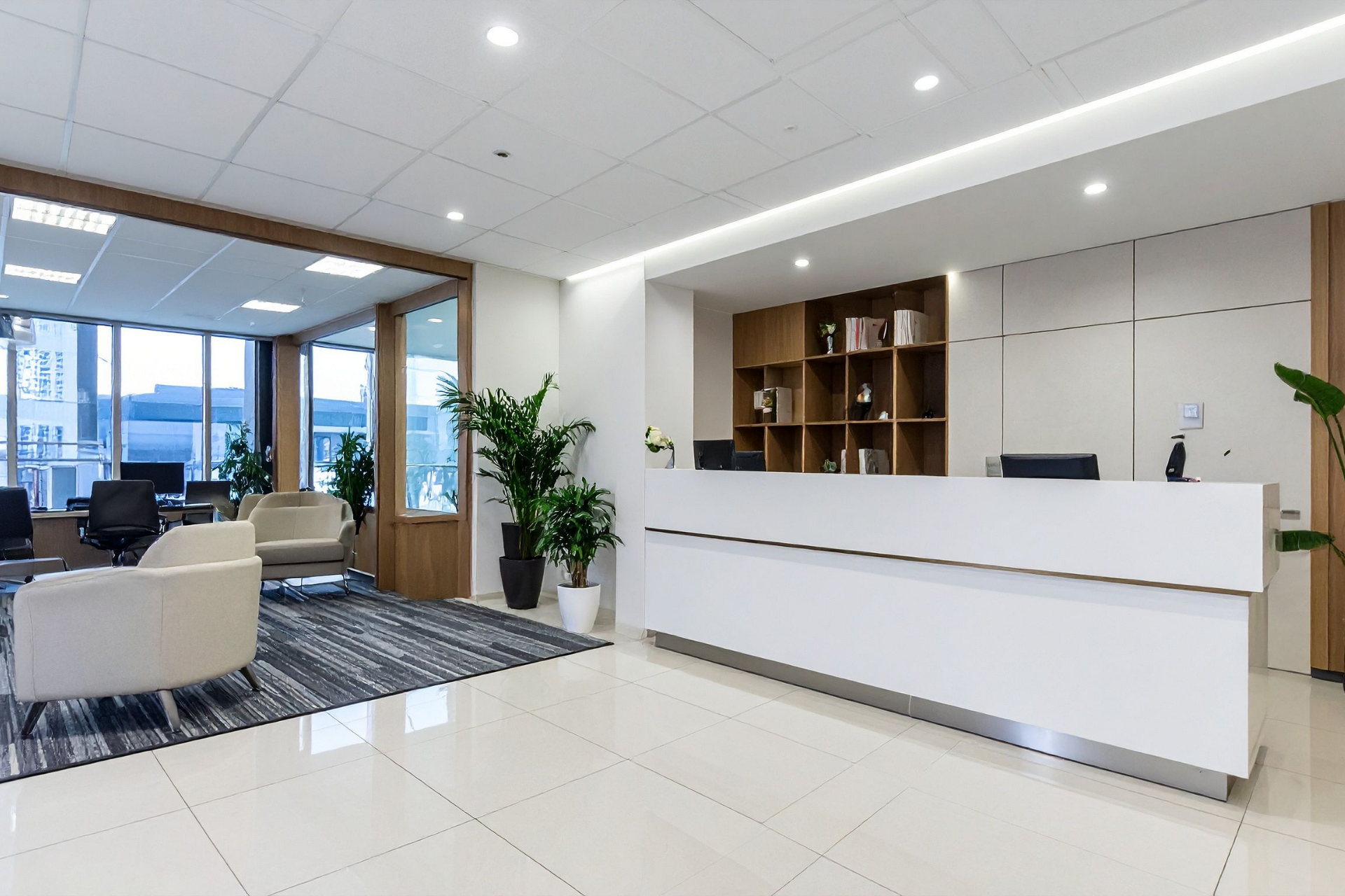 Modern office lobby with white reception desk, seating area, plants, and city view through large windows