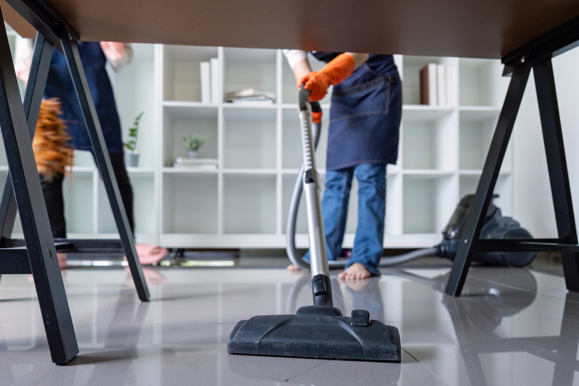 Person vacuuming a glossy office floor near shelves and desks