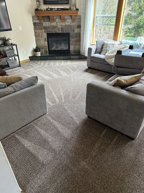 Living room with a stone fireplace, beige carpet, and two gray chairs by a large window.