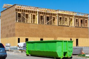 Construction site with a partly framed brick building and a bright green dumpster in front
