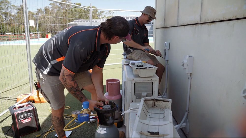 Two Men Are Working On An Air Conditioner Outside Of A Building — Entire Trades in Port Stephens, NSW