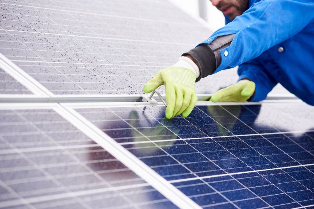 A Man Wearing Green Gloves Is Working On A Solar Panel — Entire Trades in Cessnock, NSW