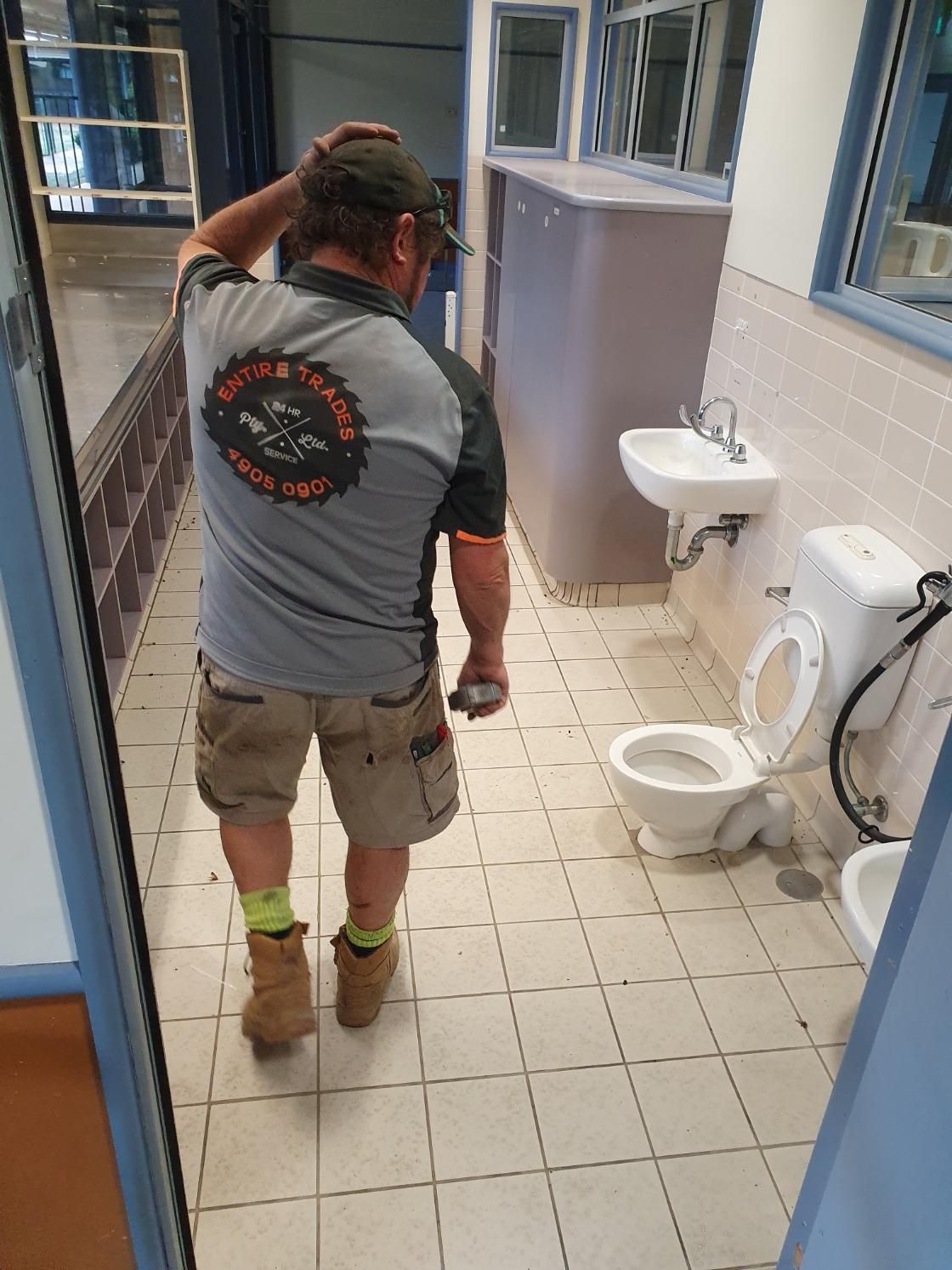 A Man Is Standing in A Bathroom with A Toilet, Sink and Mirror — Entire Trades in Singleton, NSW