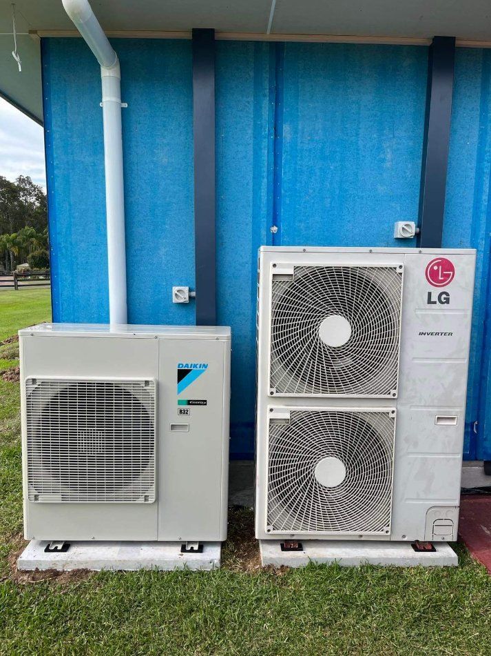 Two Air Conditioners Are Sitting Next to Each Other in Front of A Blue Building — Entire Trades in Maitland, NSW
