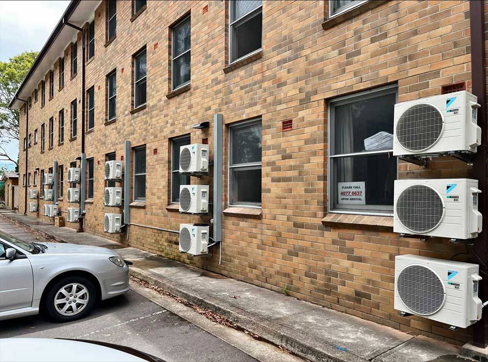  A Lot Of Air Conditioners Installed On The Brick Wall Of The Building — Entire Trades in Port Stephens, NSW