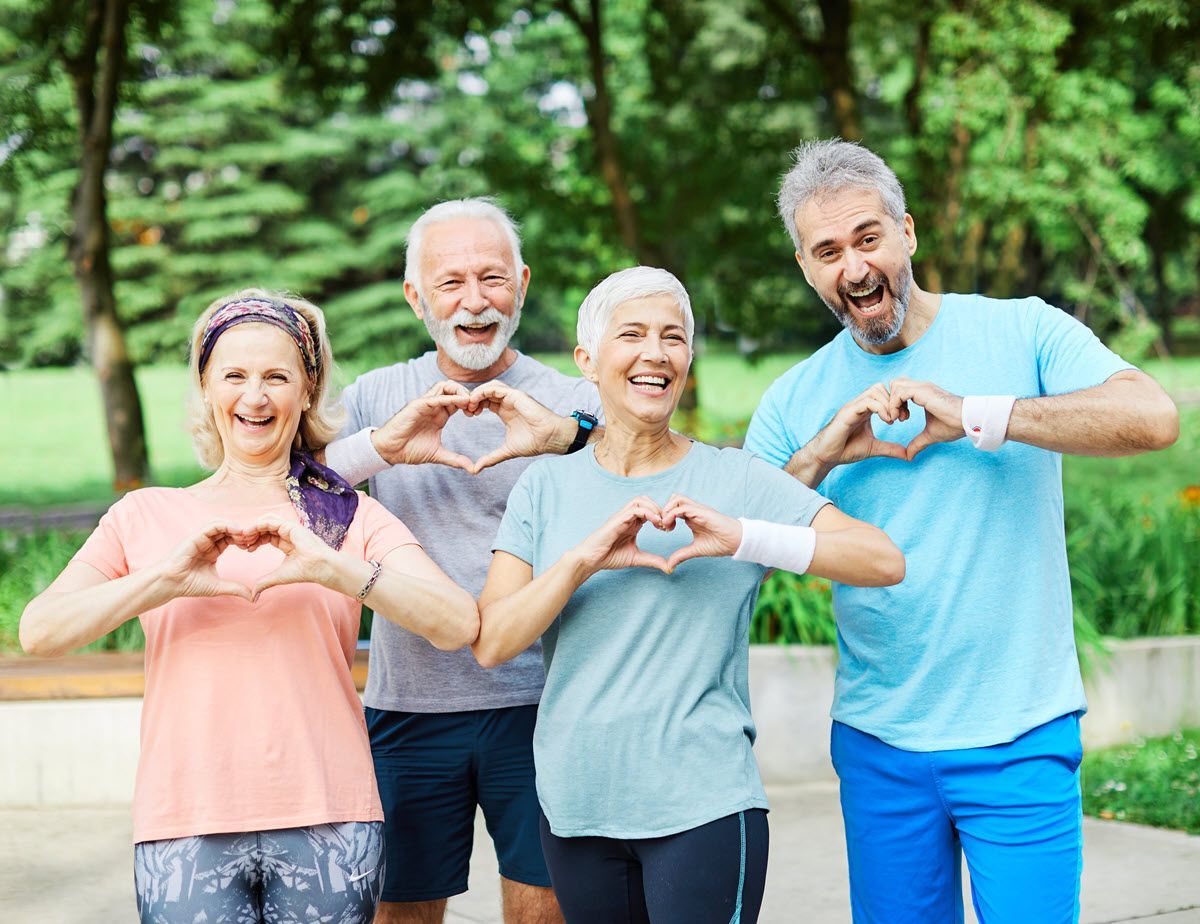 Four smiling people outdoors making heart shapes with their hands in a park.