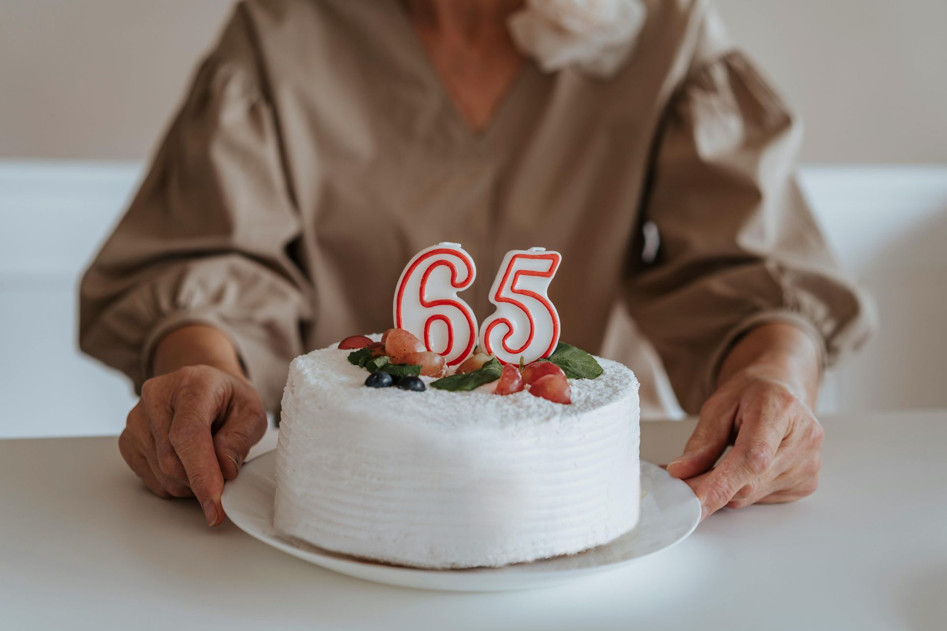 Person holding a white cake with red “65” candles on a table