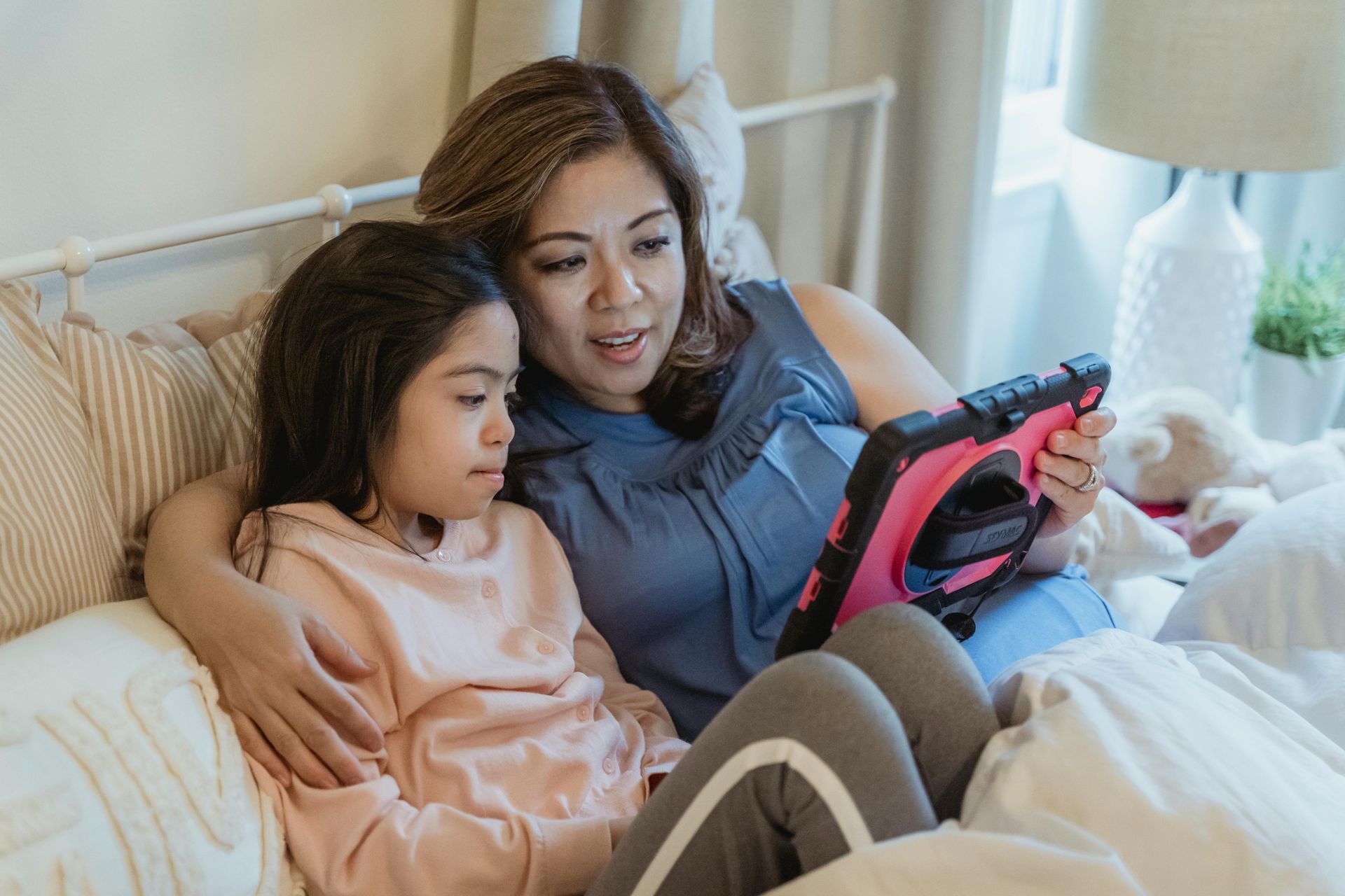 Two people sitting on a bed looking at a tablet together