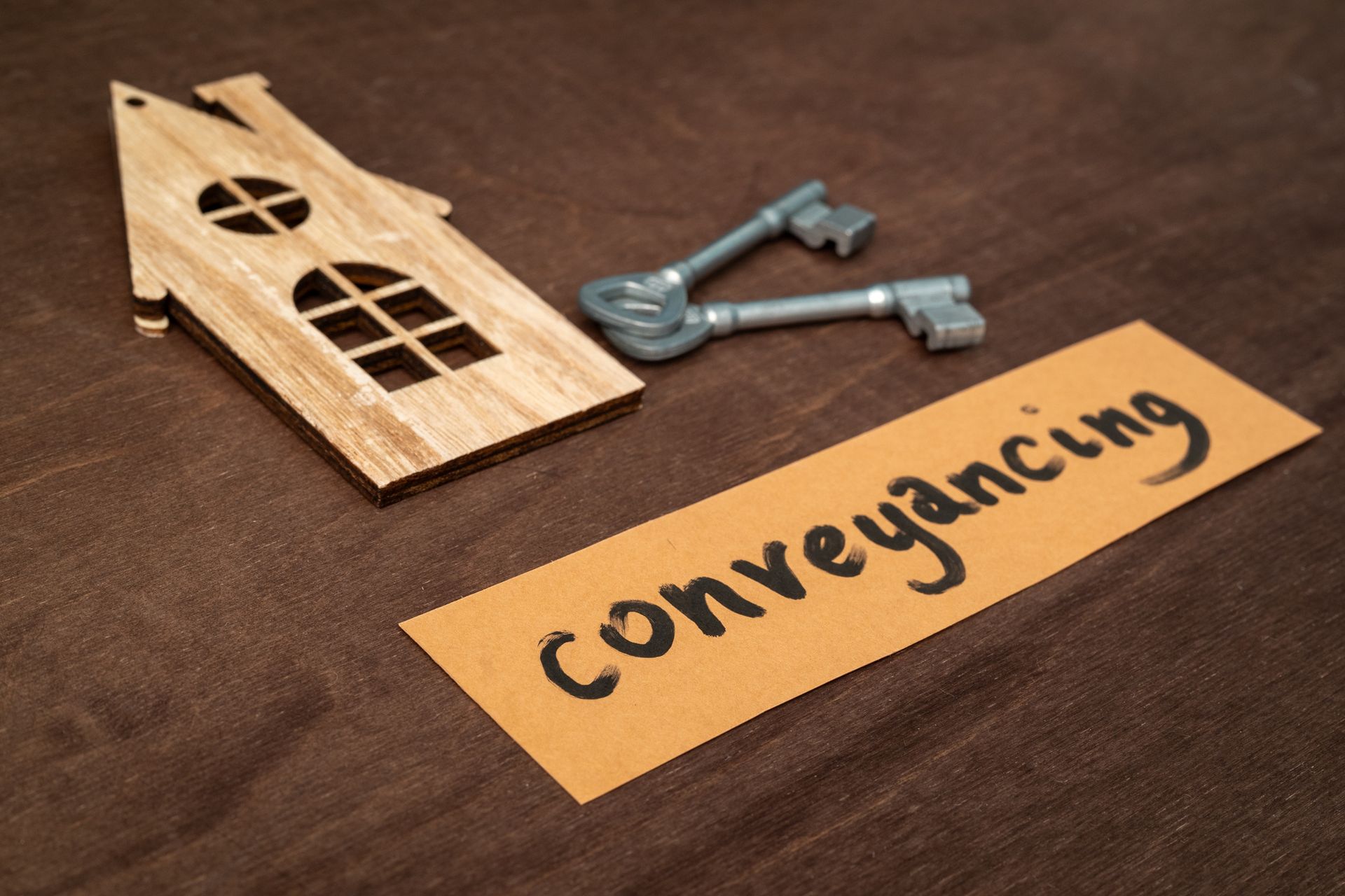 Wooden house cutout, keys, and a paper labeled 'conveyancing' on a dark wooden surface.