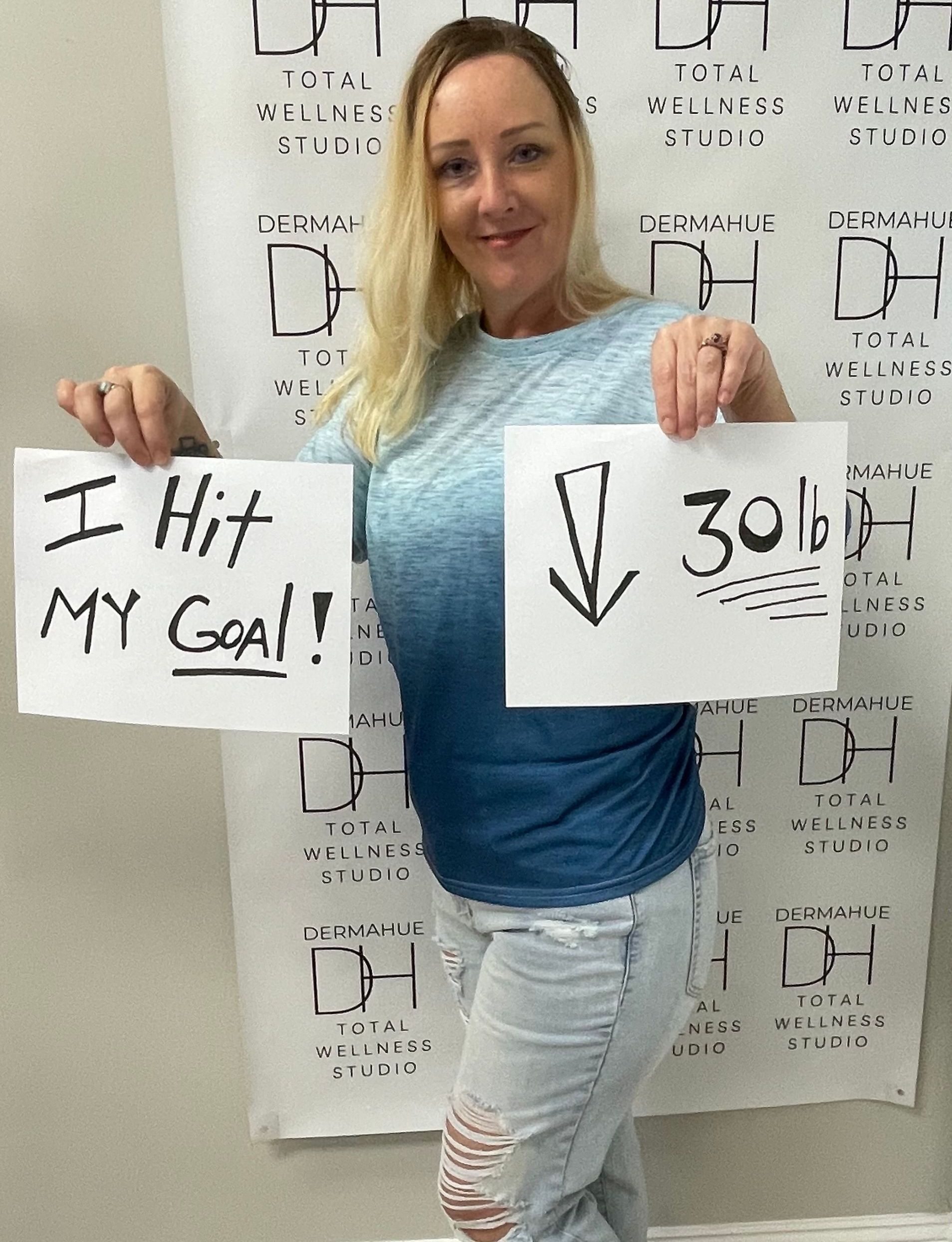 Woman holding signs: “I Hit MY Goal!” and “↓ 30 lb” in front of a patterned backdrop.