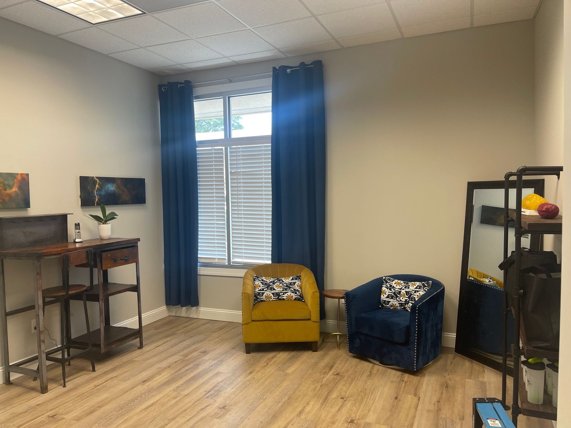 A living room with two chairs , a desk , and a window.