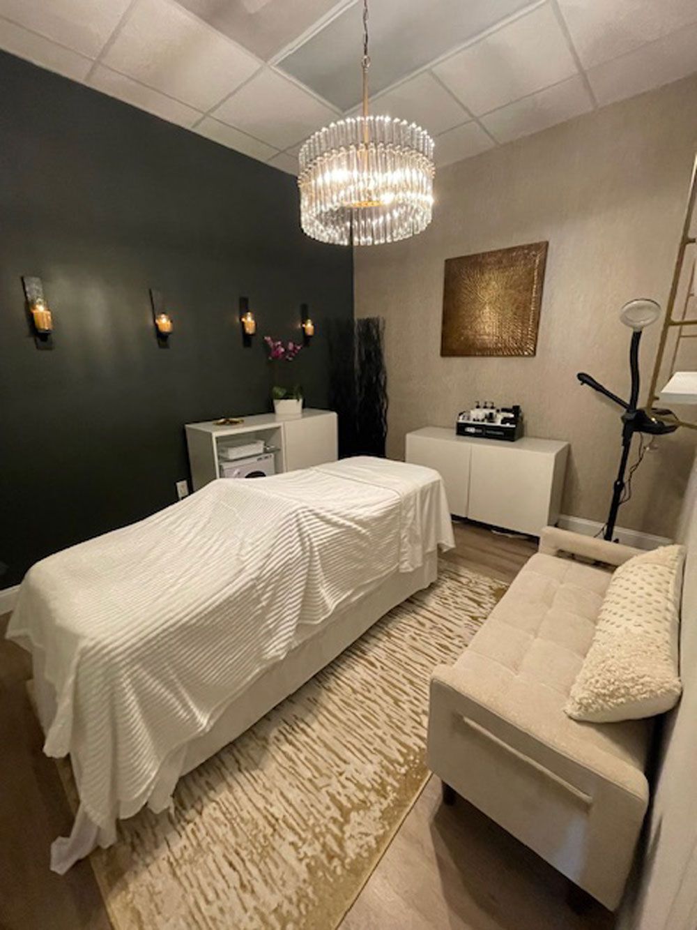 A massage room with a bed , couch , and chandelier.
