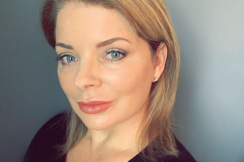 A woman with blonde hair and blue eyes is looking at the camera.