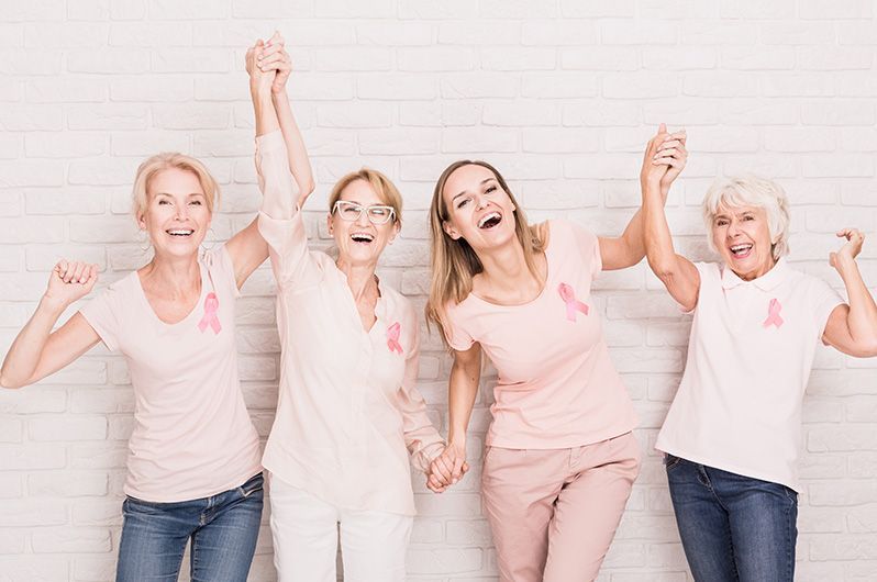 A group of women wearing pink breast cancer awareness shirts are holding hands.