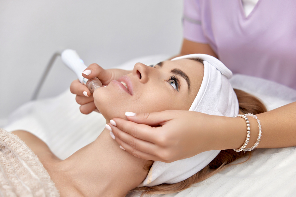 Woman receiving a facial treatment at a spa. A technician holds a device to her face.