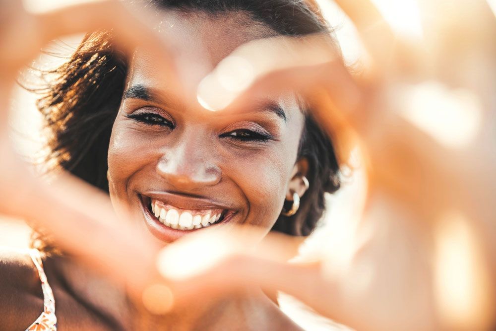 Smiling person framing their face with hands in warm sunlight