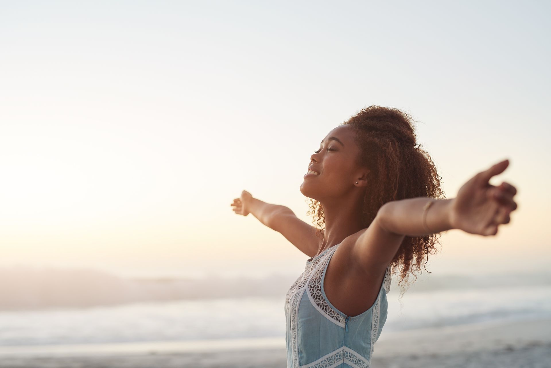 A woman is standing on the beach with her arms outstretched.