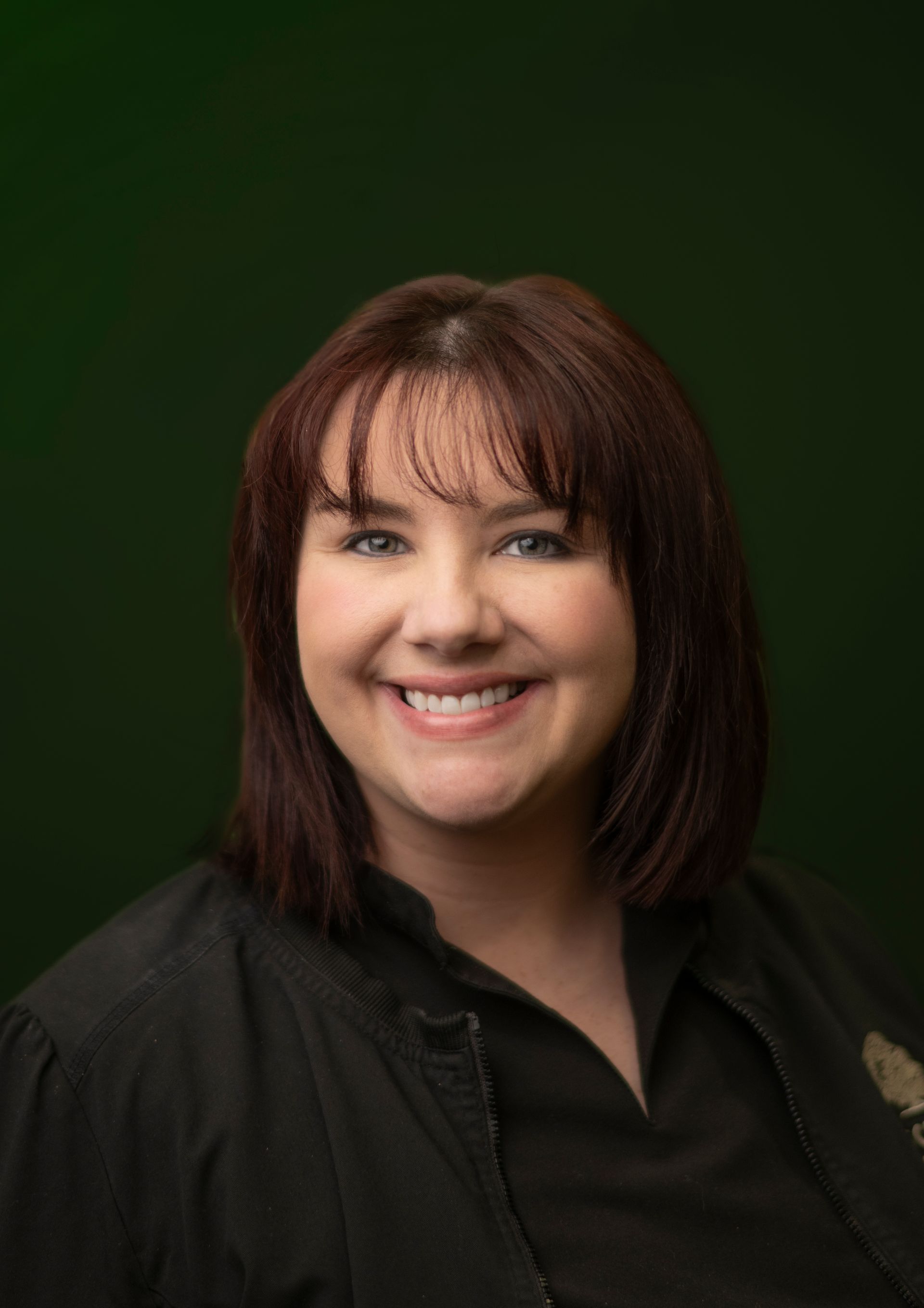 Smiling person with shoulder-length brown hair against a dark green background
