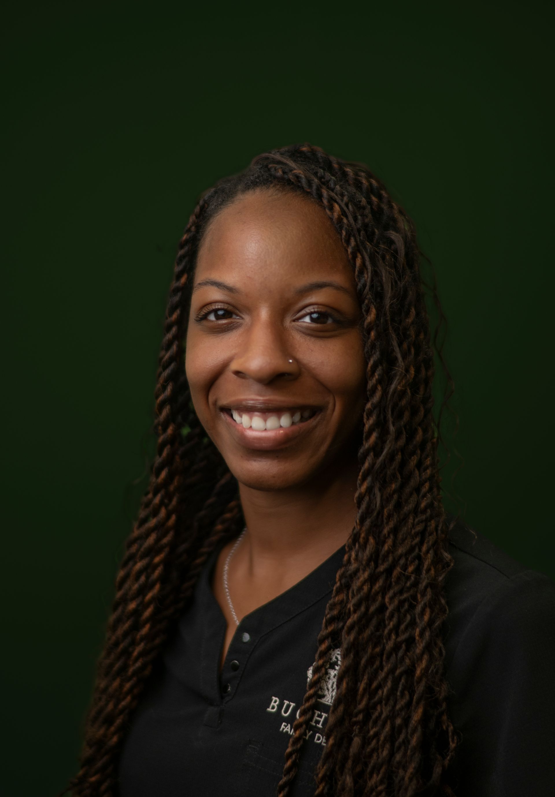 Smiling person with braided hair against a dark green background