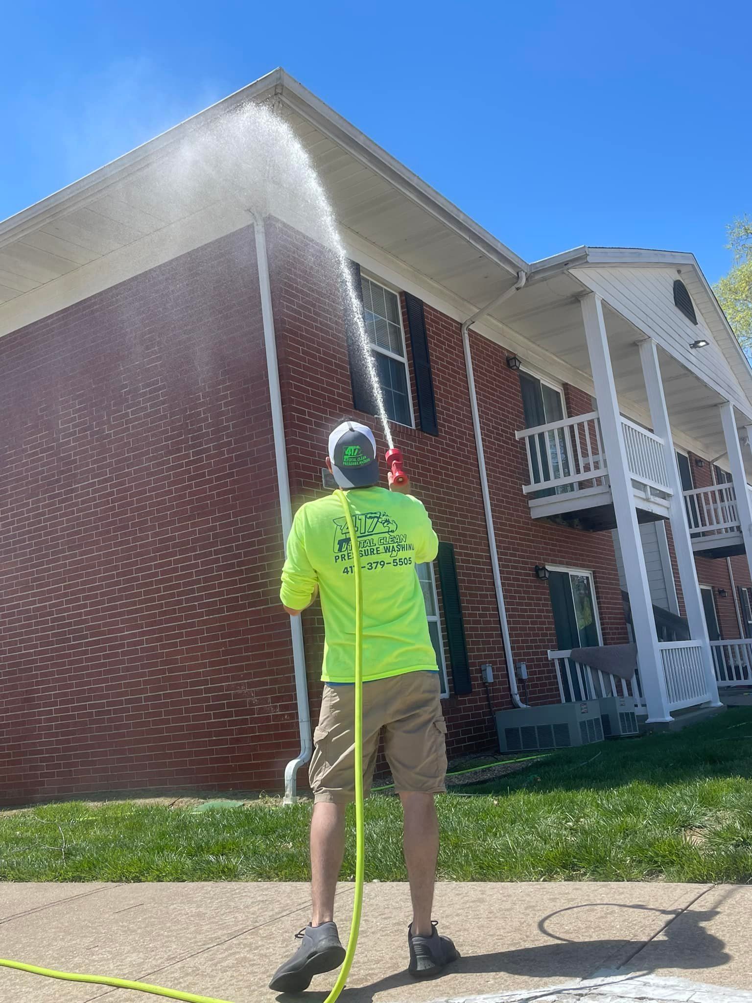 A man is cleaning the roof of a brick building with a hose.