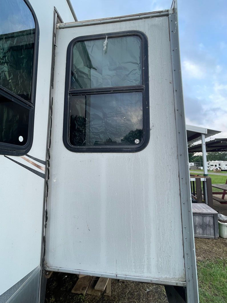 A white trailer with a broken window is parked next to a rv.