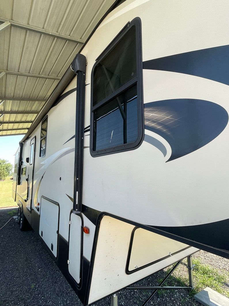 A white and black rv is parked under a roof.
