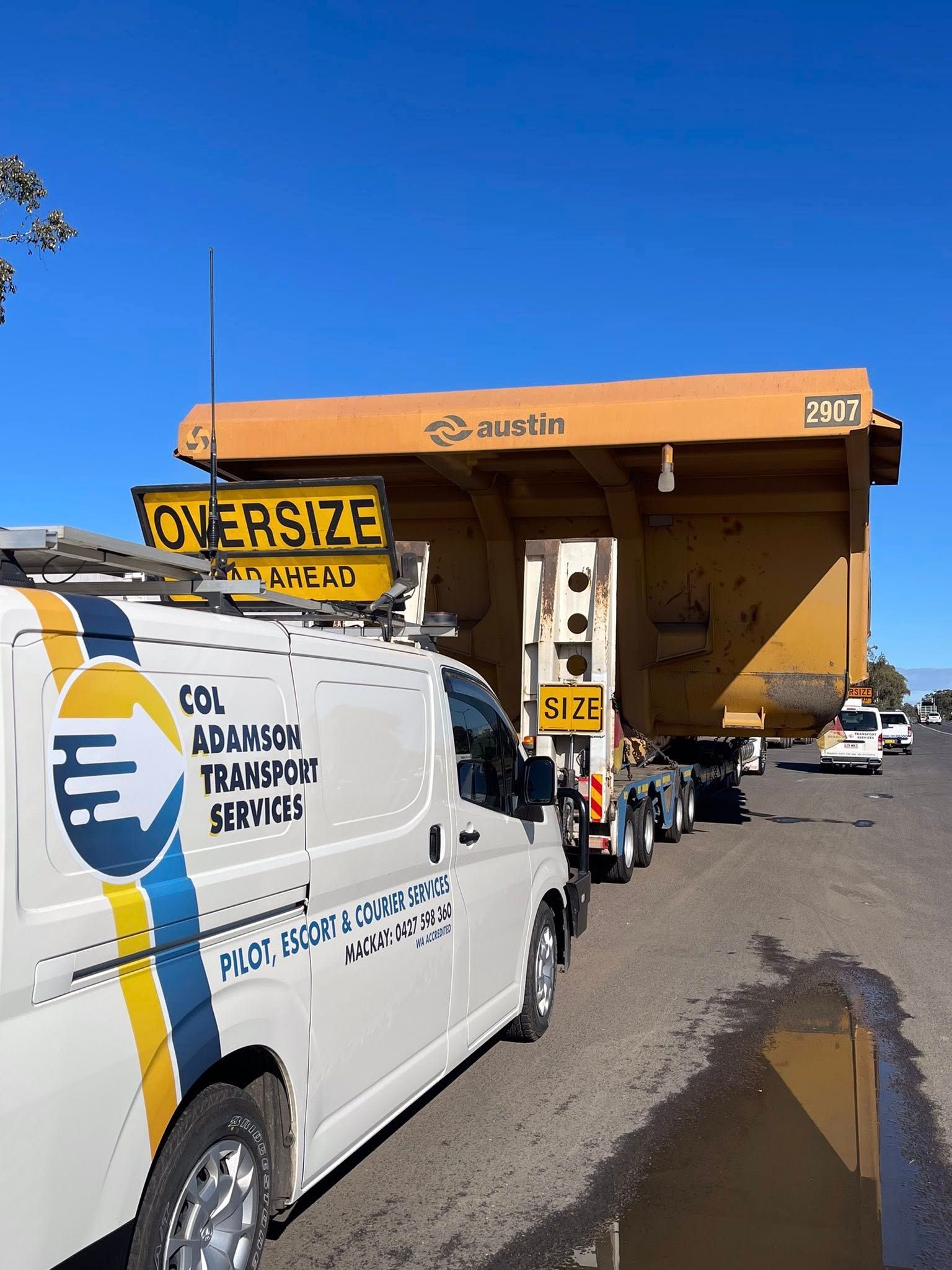 A pilot vehicle follows a flatbed truck transporting a large yellow mine dump truck bed — Col Adamson Transport Services in Farleigh, QLD