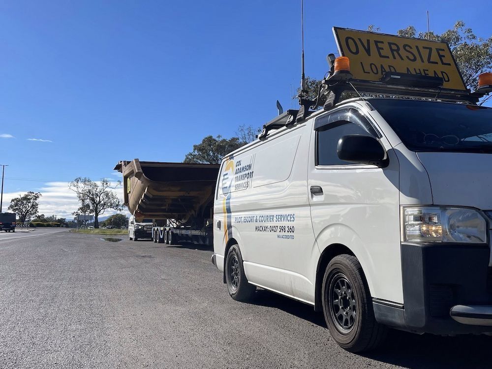 White Van With Sign Leading a Large Dump Truck on a Road Under a Blue Sky — Col Adamson Transport Services in Moranbah, QLD