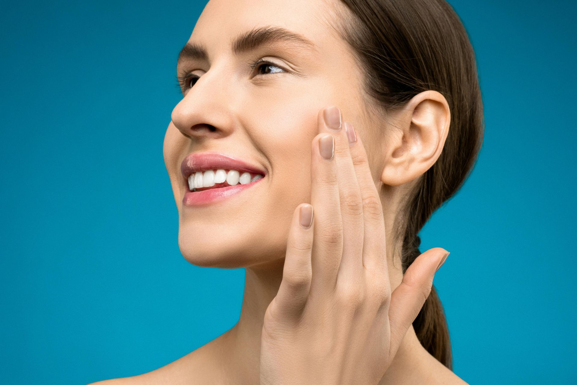 Woman applying skincare cream to her cheek against a blue background