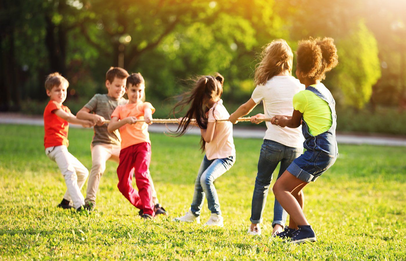Bambini che giocano al tiro alla fune su un prato verde e soleggiato.