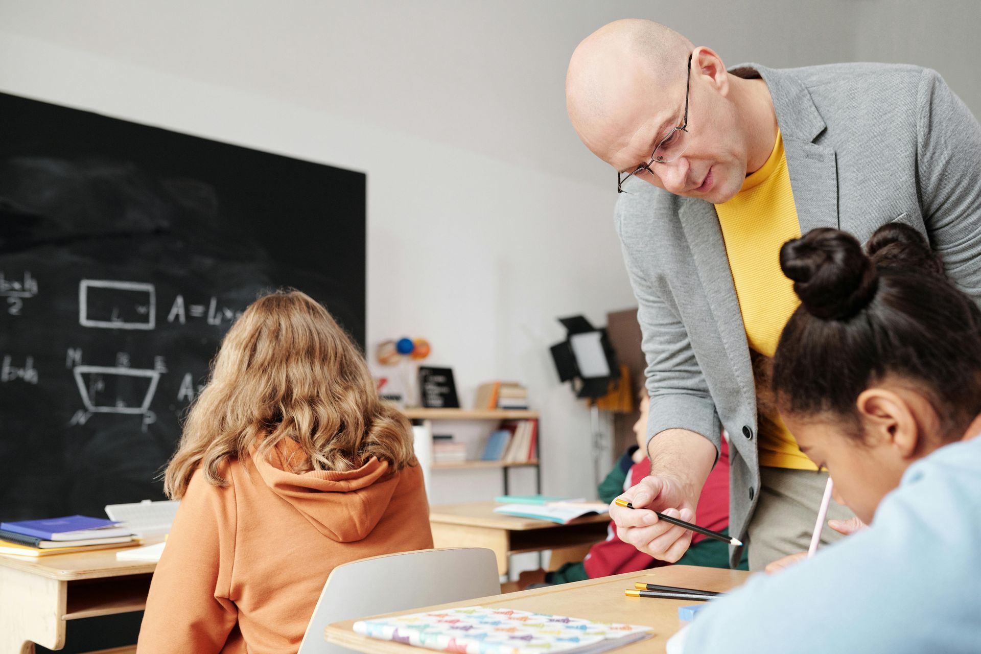 Insegnante che aiuta gli studenti ai banchi in classe. Lavagna sullo sfondo.
