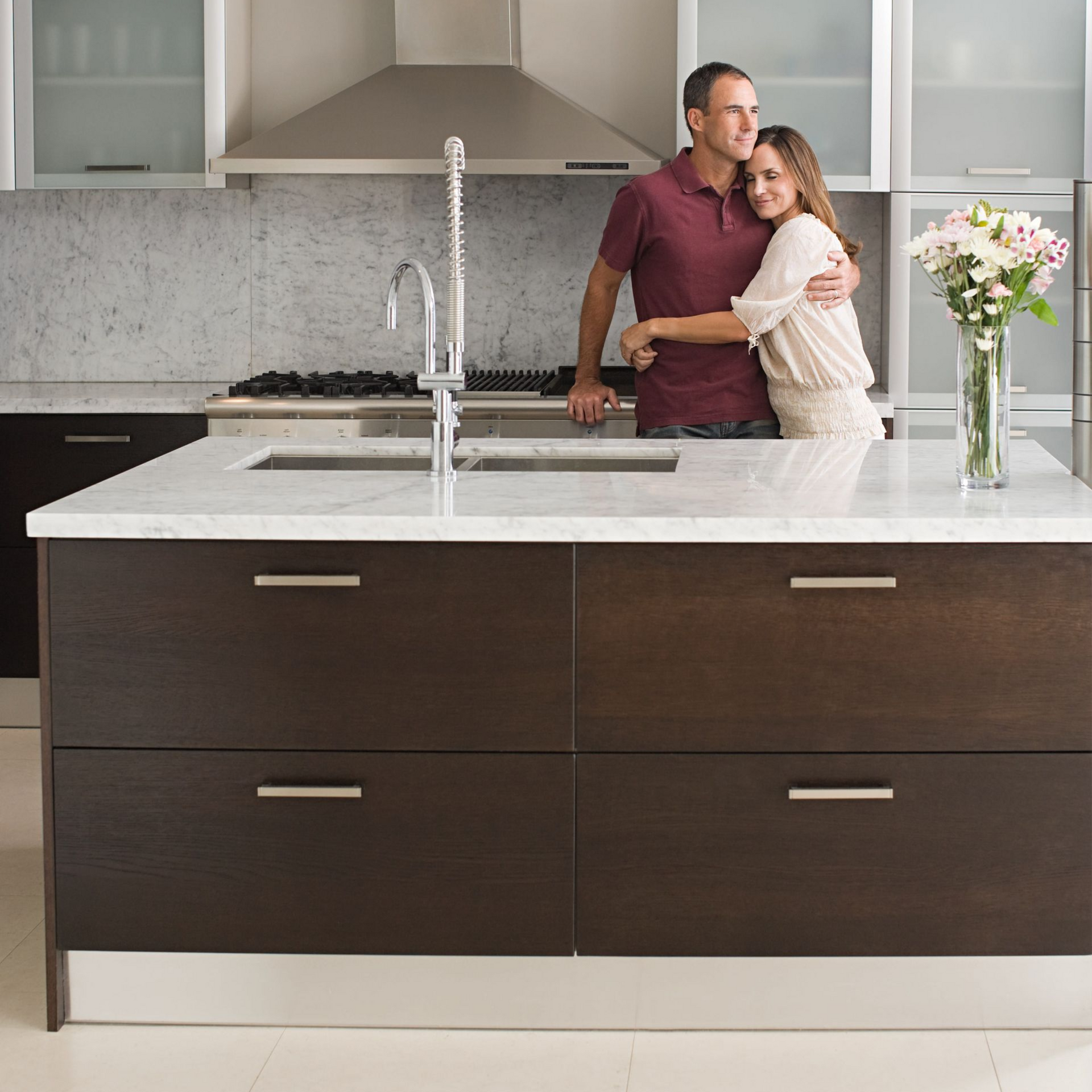Couple embracing in a modern kitchen with dark cabinets, white island, and a vase of flowers on the counter