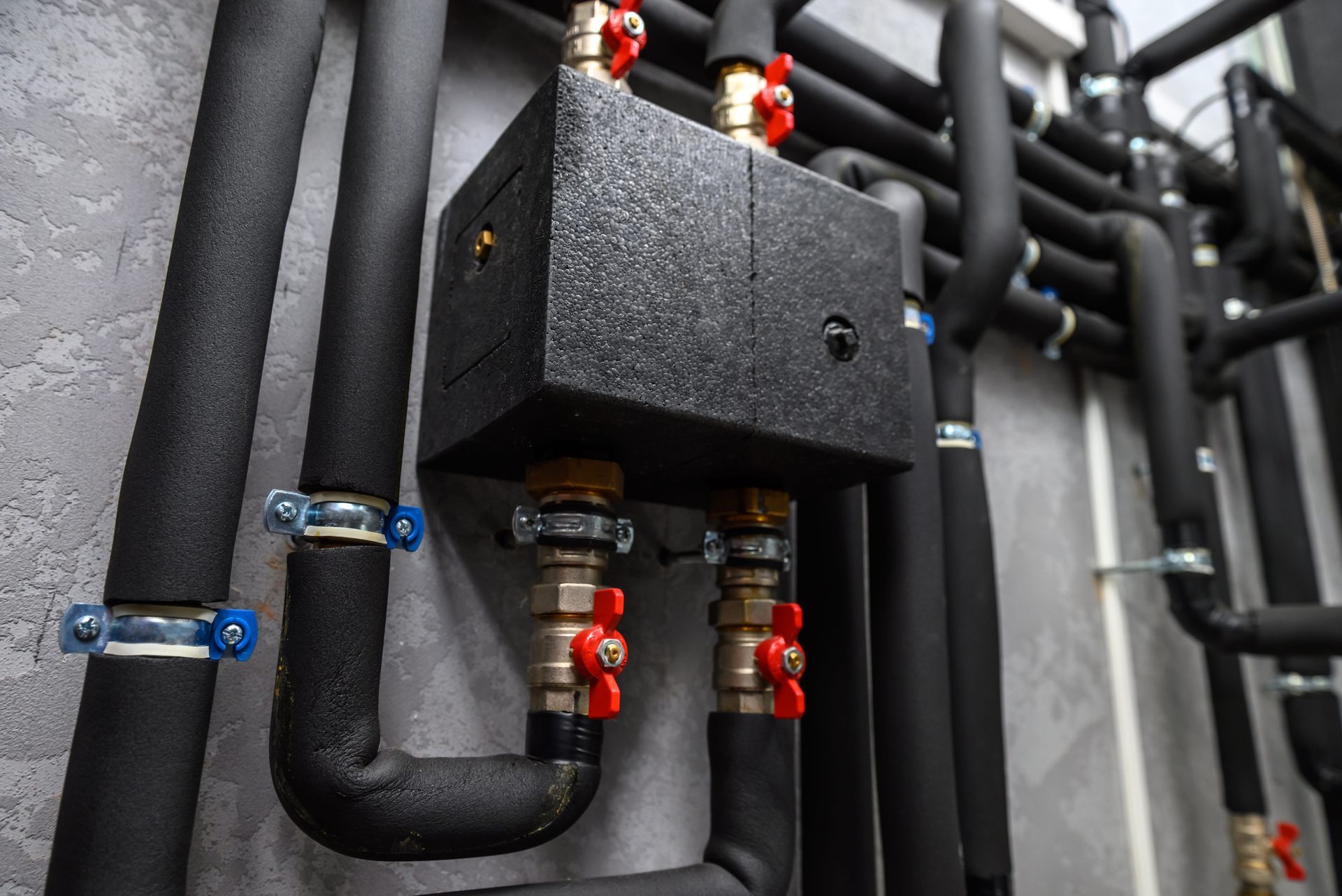 Black insulated pipes and valves connected to a metal control box in an industrial setting