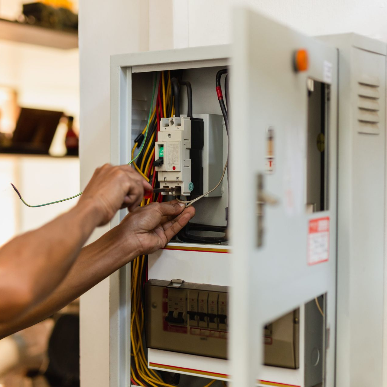 Hands adjusting wires inside an open electrical control panel box.