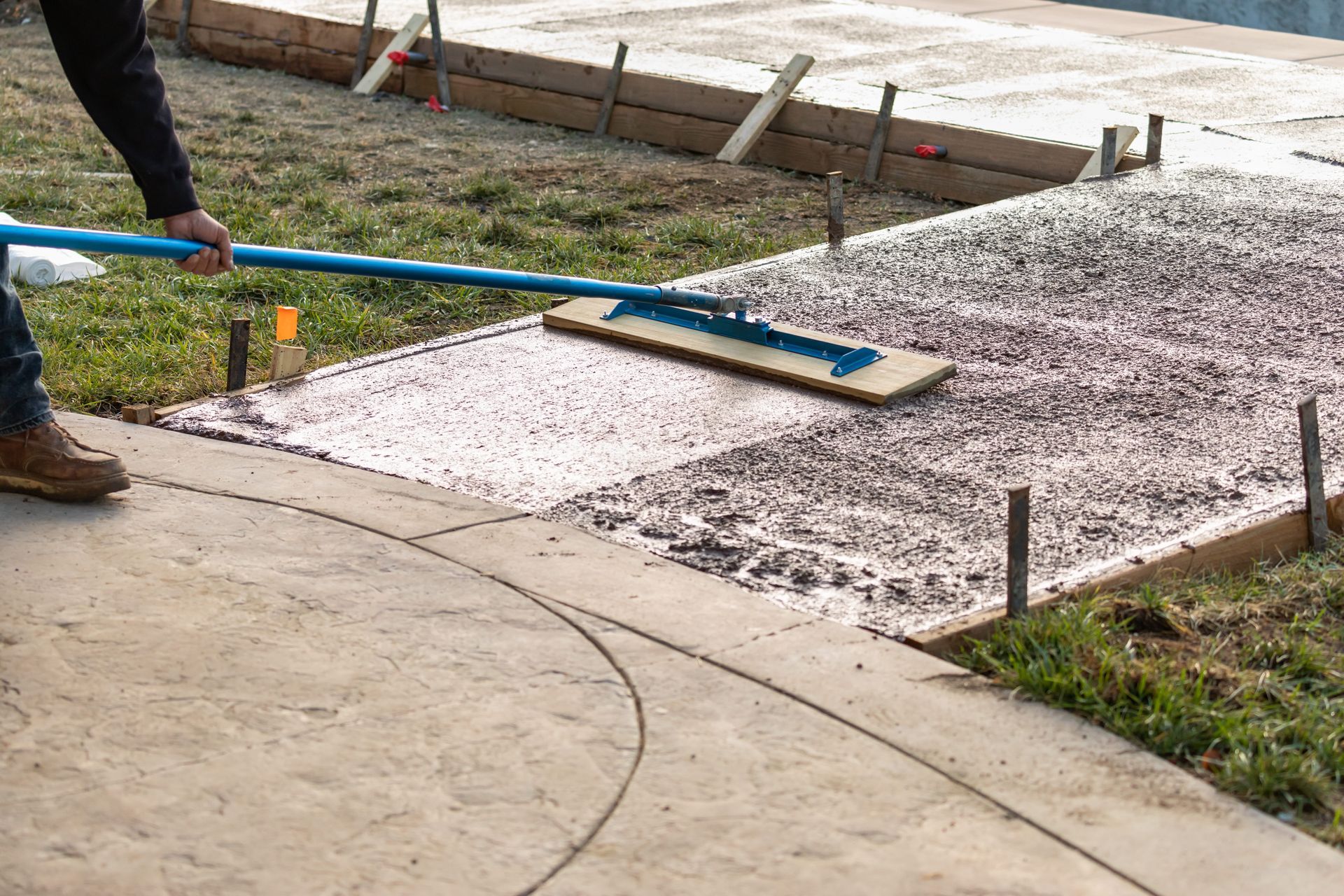Person smoothing wet concrete with a long blue tool on a sidewalk construction site