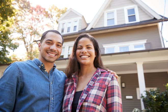 Two smiling people standing in front of a house on a sunny day