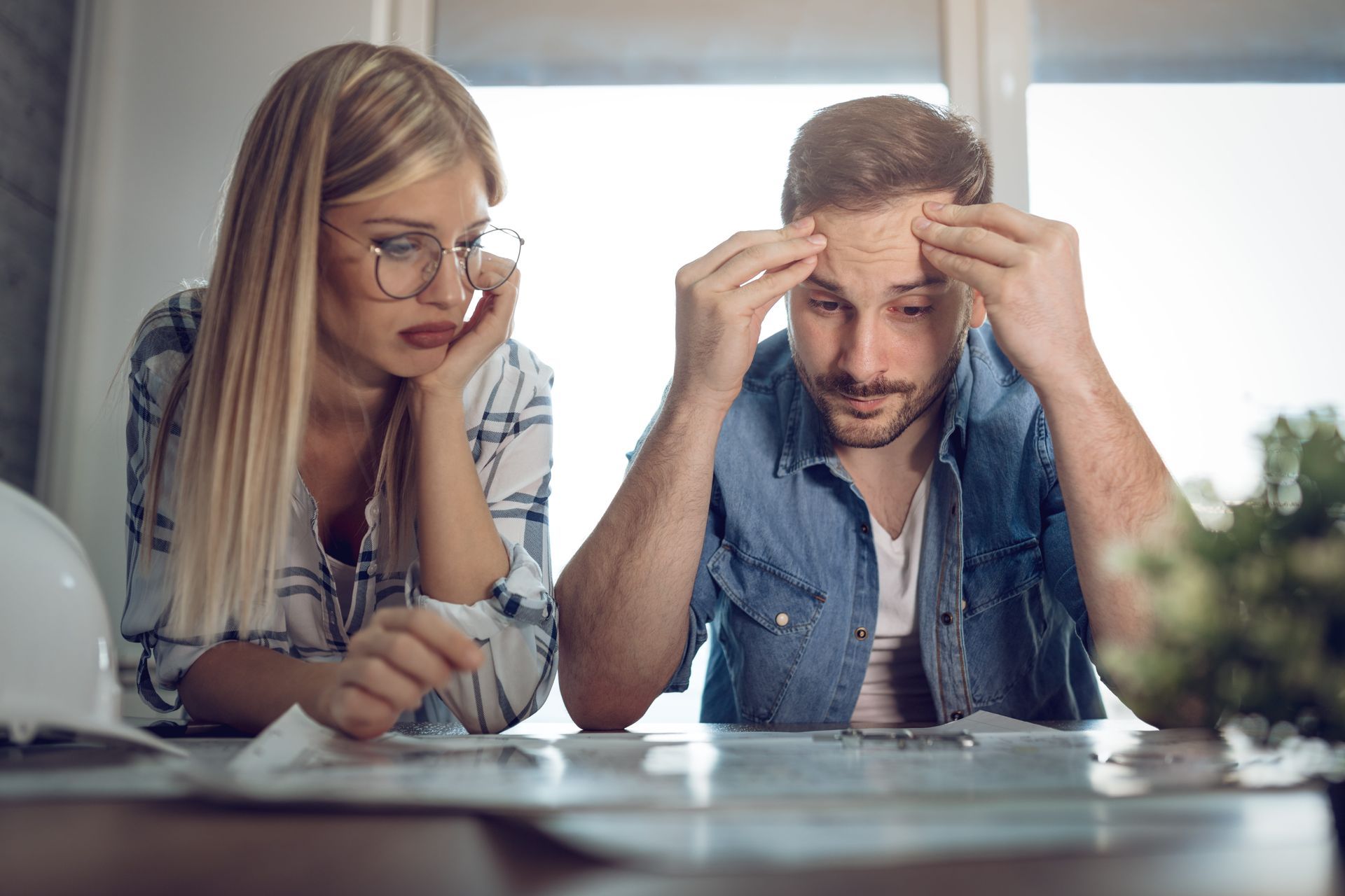 Two people reviewing paperwork at a desk, both looking stressed and concerned