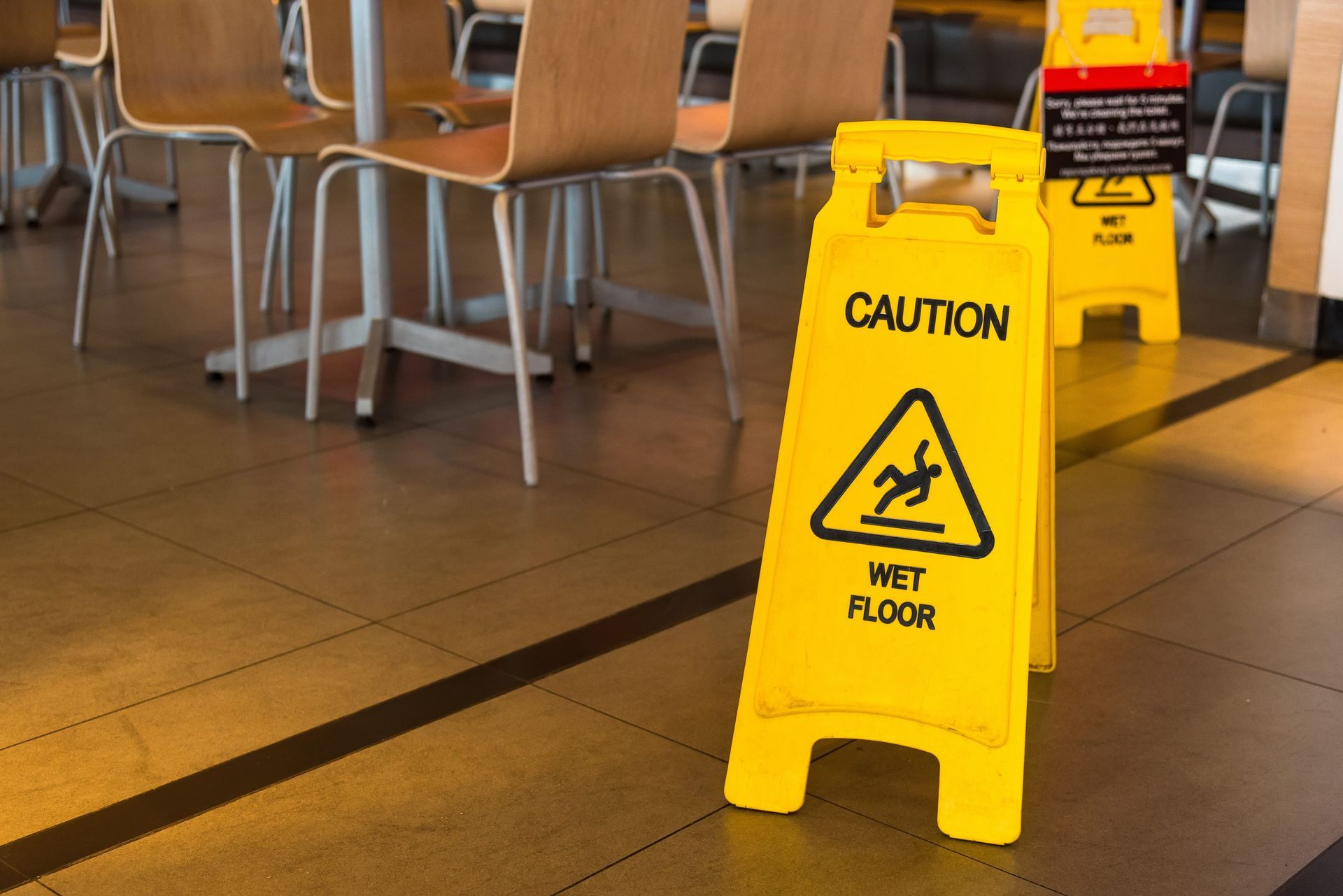 Yellow caution wet floor sign in a tiled room with chairs in the background.