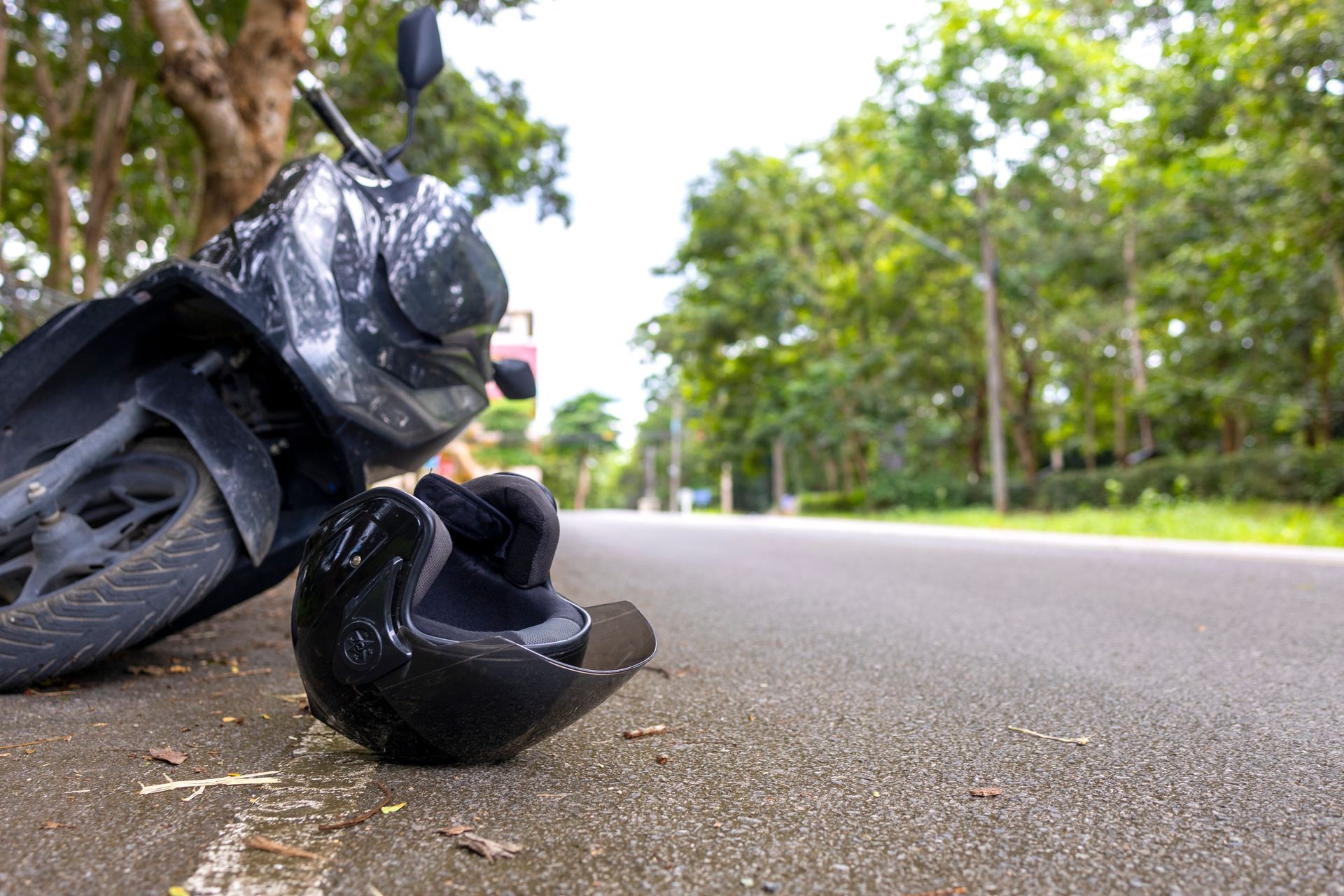 Damaged motorcycle lying on its side on a roadside, with debris scattered on the pavement.