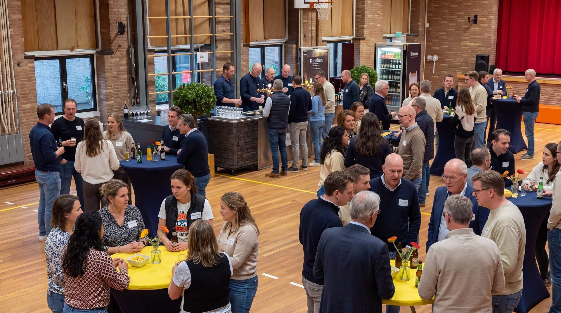 Mensen mengen zich onder elkaar tijdens een levendige receptie binnen met ronde tafels, drankjes en bakstenen muren.