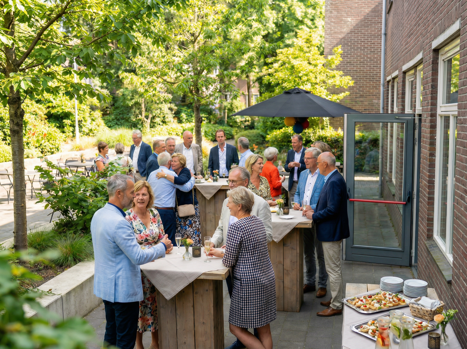 Gasten mengen zich onder elkaar op een terras buiten, naast een bakstenen gebouw, waar drankjes en hapjes op tafels staan.