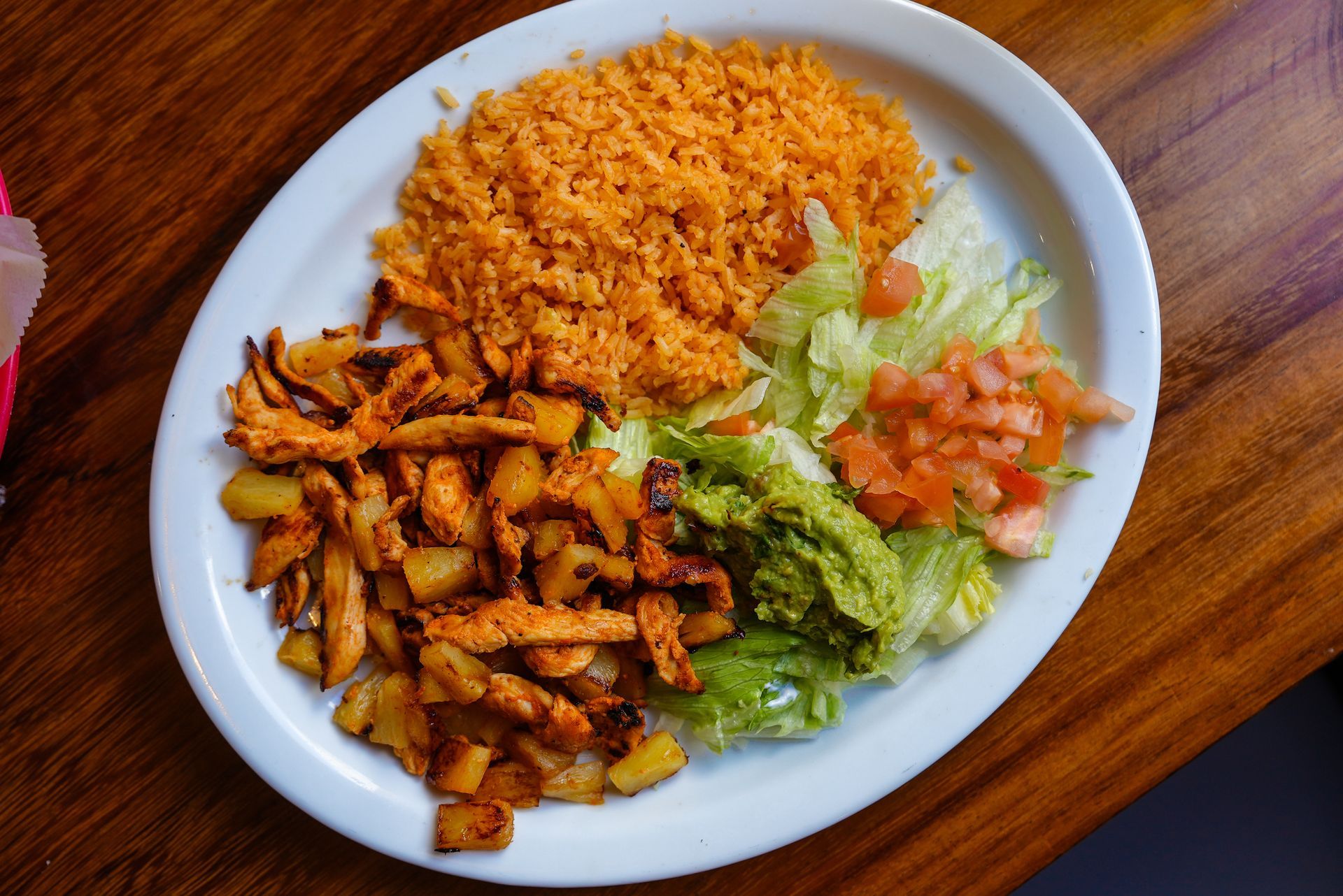 A white plate topped with rice chicken guacamole and lettuce