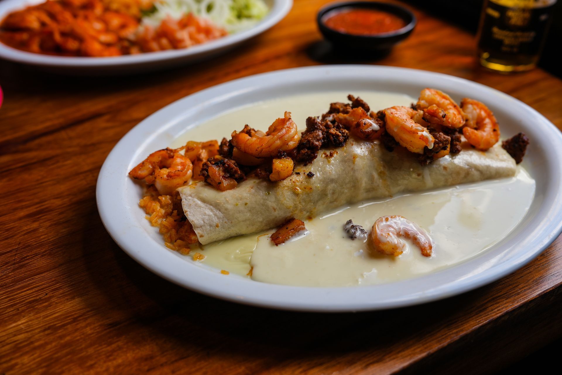 A burrito with shrimp and meat on a white plate