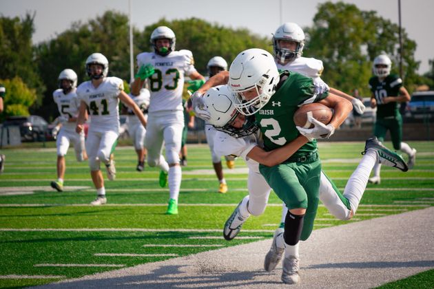 Football player in silver uniform runs with ball on a green field.