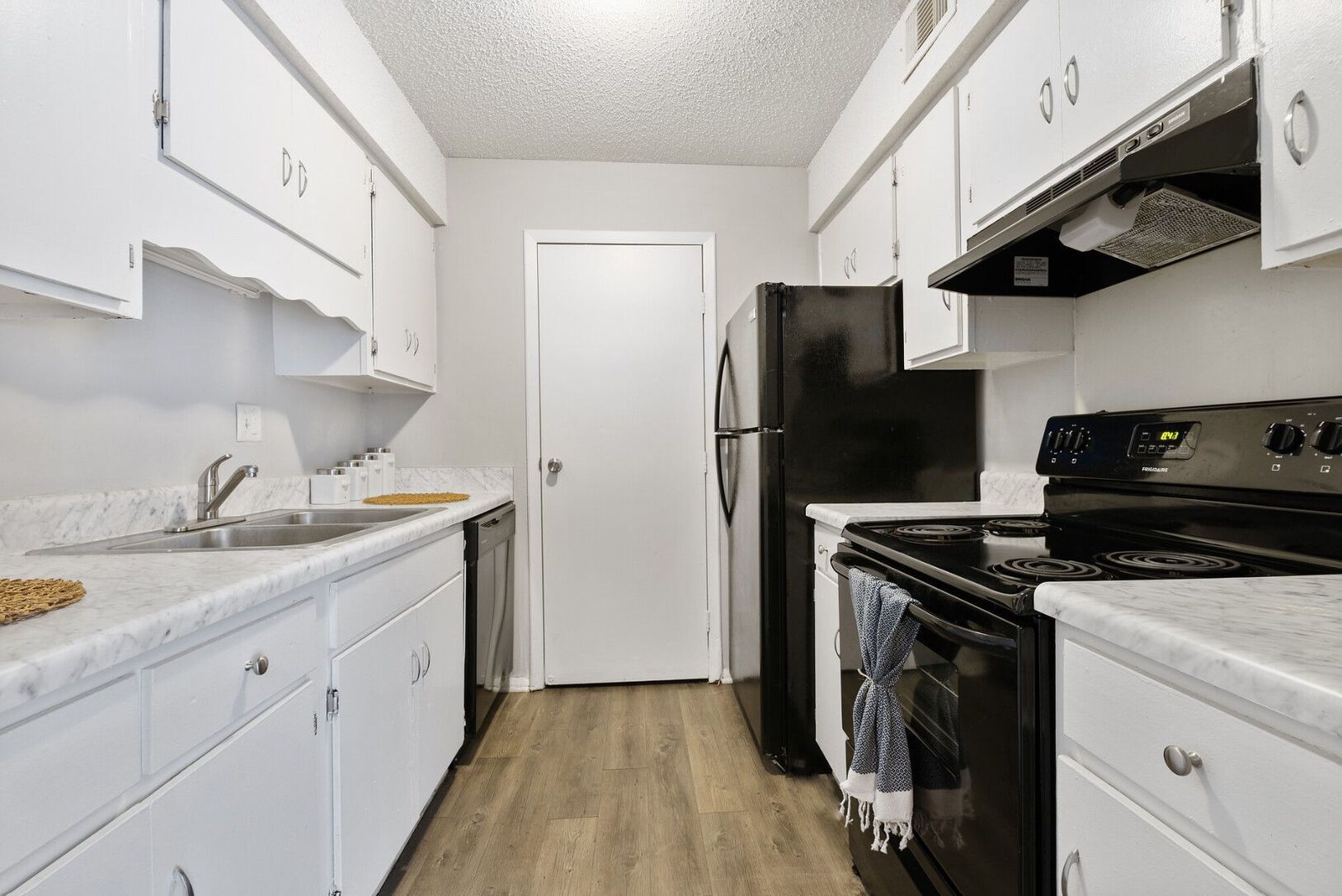 White kitchen with white cabinets, black appliances, and a door at the end.